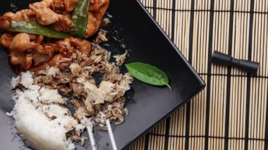 Siyah tabakta pilavlı kızarmış tavuk ve çubuk.