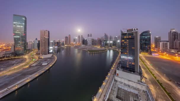 迪拜商业湾摩天大楼的城市景观与水渠空中夜间到日间的过渡全景时间与月亮落山 有照明塔和海滨的现代天际线 — 图库视频影像