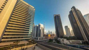 Gündoğumunda Dubai şehir merkezi ve difc gökdelenlerine bakan hava panoramik, Business Bay zaman dilimindeki kavşakta yoğun bir trafik var. Güneş, kulelerdeki cam yüzeyden yansıyor