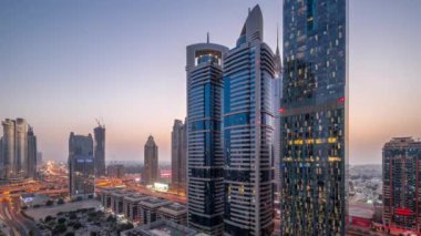 Günbatımından sonra Dubai Uluslararası Finans Bölgesi 'nin hava görüntüsü ve birçok gökdelen gece gündüz geçiş zamanı. Otoparkın yanındaki kavşakta trafik vardı. Dubai, BAE.