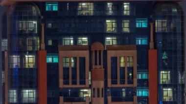 Aydınlatılmış çalışma odası saatleriyle apartman penceresi ön cephesinin gece görüşü. Gökdelende parlayan ışık