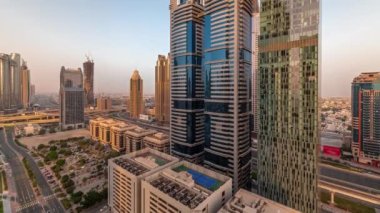 Dubai Uluslararası Finans Bölgesi 'nin birçok gökdelen zaman ayarlı sabah görüntüsü. Gün doğarken uzun gölgeli çok katlı otoparkın yakınındaki bir yolda trafik vardı. Dubai, BAE.