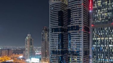 Panorama, Dubai Uluslararası Finans Bölgesi 'nin gökdelenler tarafından aydınlatılmış gece zaman çizelgesini gösteriyor. Çok katlı otoparkların yakınındaki bir yolda trafik vardı. Dubai, BAE.