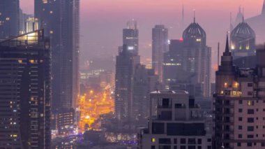 Dubai Marina ve Media City semtleri modern gökdelenler ve ofis binaları gece gündüz geçiş zamanları. Limandaki yatların yakınındaki üst geçitte trafik ve kavşak.