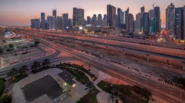 Dubai Marina gökdelenleri ve Şeyh Zayed yolu ile metro demiryolu havadan geceye geçiş panoramik zaman çizelgesi. Günbatımından sonra modern kulelerin yakınındaki bir otoyolda trafik, Birleşik Arap Emirlikleri