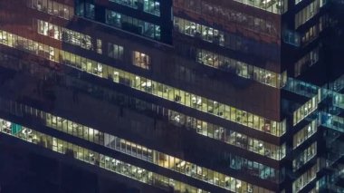 Yüksek katlı ofis binasının pencereleri gecenin geç saatlerinde parlayan ve yanıp sönen iç ışıkları olan dış kısımda. Havadan üst görünüm