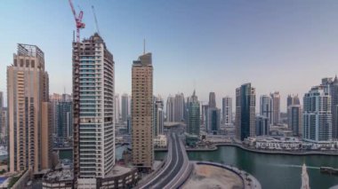 Dubai Marina gezinti güvertesi ve kanalı, gün batımından sonra Dubai, BAE 'de yüzen yatlar ve teknelerle hava üzerinden gece gündüz geçiş zamanı. Modern kuleler ve yol trafiği