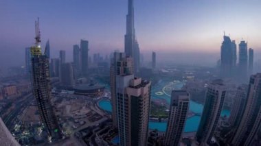 Dubai şehir merkezinde sisli bir sabah, gece gündüz geçiş panoramik zaman dilimi. Şehrin sislerle ve çeşmelerle kaplı gökdelenlerinin gelecekteki manzarası. Çatıdan gün doğumuyla birlikte hava manzarası. Dubai, BAE