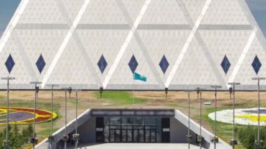 Barış ve Uzlaşma Sarayı 'nın dışında park ve fıskiyelerle birlikte zaman ayarlı bir bina var. Nur-Sultan şehri, Kazakistan.