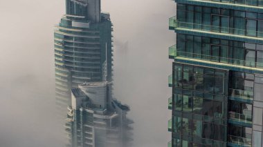 Dubai Marina ufuk çizgisi üzerinde nadir bulunan kış sisi ve hava saatleri üzerinde cam gökdelenlerle kaplı kuleler. Üst görünüm bulutların üstünde. Dubai, BAE
