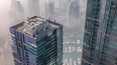 Modern gökdelenler, hava zaman çizelgeleri ve Dubai Marina 'nın sabah puslu su iskelesi, Birleşik Arap Emirlikleri. Yatlar ve kayıklar cam kuleler arasında