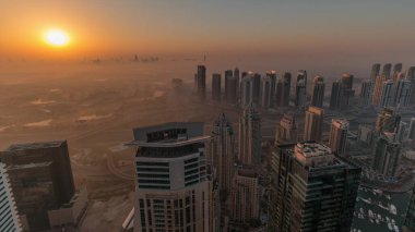 Dubai Marina Panoraması 'nda güneş doğarken JLT gökdelenleri ve golf sahası, Dubai, Birleşik Arap Emirlikleri. Yukarıdan hava manzarası sisli bir sabah. Turuncu gökyüzü ile şehir silueti