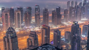 Şeyh Zayed Yolu yakınlarındaki JLT gökdelenleri ve marina kuleleri gece gündüz geçiş zamanı. Aydınlatılmış konut binaları ve villalarla ufuk çizgisi. Güneş doğmadan önce sisli bir sabah