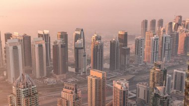 Güneş doğarken Şeyh Zayed Yolu yakınlarındaki JLT gökdelenleri ve marina kuleleri. Konut binaları ve villalı ufuk çizgisi. Sıcak turuncu ışıkla gün doğumunda sisli bir sabah
