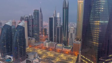 Dubai 'nin finans merkezi, gece gündüz aydınlık lüks gökdelenler geçiş zamanı, Dubai, Birleşik Arap Emirlikleri. Otoparkı ve çatısı olan hava manzarası