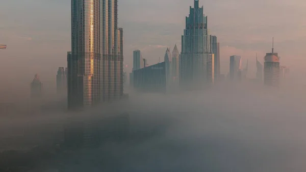 霧のタイムラプスの間のドバイ市内早朝の空中ビュー 高層ビルや塔がある未来的な都市のスカイラインで日の出 ガラス面から反射した太陽 — ストック写真
