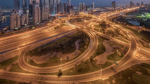 stock image Panorama of Dubai Marina highway intersection spaghetti junction night to day transition timelapse. Illuminated tallest skyscrapers and golf course on a background. Aerial top view from JLT district before sunrise