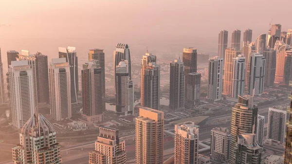 JLT skyscrapers and marina towers near Sheikh Zayed Road aerial timelapse during sunrise. Residential buildings and skyline with villas. Foggy morning during sunrise with warm orange light