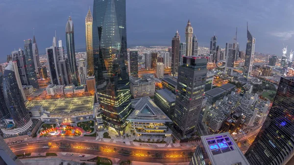 Panorama of futuristic skyscrapers in financial district business center in Dubai with road traffic night to day transition timelapse. Aerial view from above with illuminated towers during sunrise