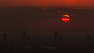 Sebze üzerinden gün doğumu ve Dubai marinasından Al Barsha Tepeleri hava zaman çizelgesi. Golf sahasının yakınındaki kulelerin ve gökdelenlerin arkasından güneş yükseliyor.