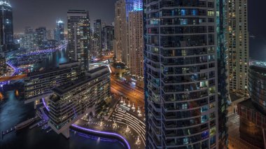 Panorama Dubai marinasının hava manzarasını gösteriyor. Kanal etrafındaki gökdelenleri aydınlatıyor. Yüzen yatlar ve gece saatleri var. Jlt ve JBR bölgelerindeki kuleler. Yat kulübünde beyaz tekneler var.