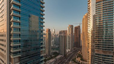 Dubai Marina ve JBR bölgesi ve caddelerdeki trafik sabah saatleri ve güneş gün doğumunda sisli gökdelenlerden yansıyor.