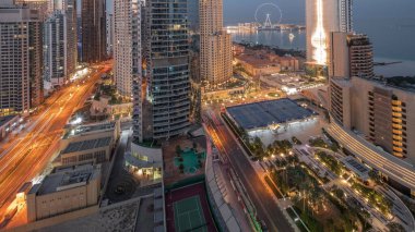 Dubai Marina ve JBR bölgesinin panoramik görüntüsü ve ünlü dönme dolabın gece gündüz geçiş zamanı. Gün doğumunda uzun gölgelerle aydınlatılmış gökdelenler