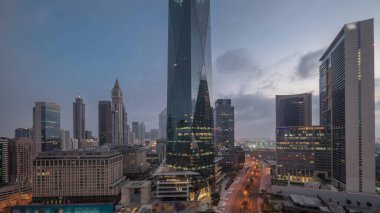 Dubai International Financial district night to day transition timelapse. Panoramic aerial view of business office towers before sunrise. Illuminated skyscrapers with hotels near downtown clipart