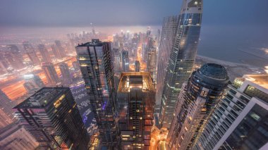 Dubai Marina 'nın ufuk çizgisi panoramik manzarası kıyı şeridi boyunca aydınlık gökdelenlerle çevrili kanalı gösteriyor. Gece gündüz geçiş zamanı. Güneş doğmadan önce sisli bir hava. Dubai, BAE