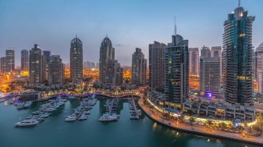 Gündoğumundan önce Dubai marinasında gece gündüz lüks yat hangarında geçiş zamanı. Rıhtım boyunca modern gökdelenler ve limanda yüzen tekneler.