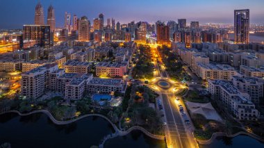 Barsha Heights bölgesindeki gökdelenler ve Greenens bölgesindeki alçak binalar gece gündüz panoramik zaman atlamaları. Palmiyeler ve ağaçlarla Dubai silueti