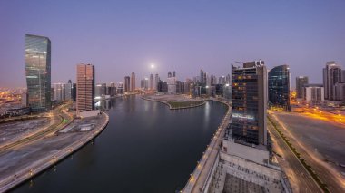 Dubai İş Körfezi 'ndeki gökdelenlerin şehri. Gece gündüz su kanalları havası. Ay batarken panoramik zaman geçişi. Gündoğumundan önce aydınlık kuleleri ve rıhtımı olan modern gökyüzü.