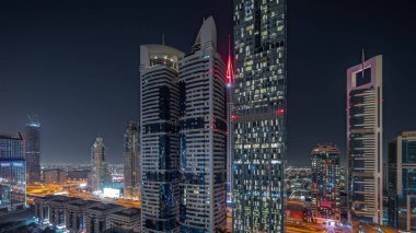 Panorama, Dubai Uluslararası Finans Bölgesi 'nin gökdelenler tarafından aydınlatılmış gece zaman çizelgesini gösteriyor. Çok katlı otoparkların yakınındaki bir yolda trafik vardı. Dubai, BAE.