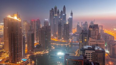 Dubai Marina hava sahasının en yüksek bloğundaki çeşitli gökdelenlerin görüntüsü. Gece gündüz yapay kanalla geçiş zamanı. Güneş doğmadan önce birçok kule ve yat sisli.