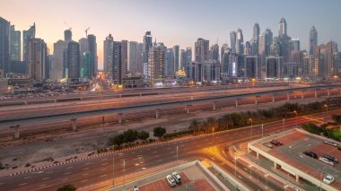 Dubai marinası gökdelenlerin en uzun bloğu günden geceye geçiş zamanı. JLT bölgesinden apartman binalarına, otellere ve otoyol ve metro hattı yakınlarındaki iş kulelerine hava panoramik görüntüsü.