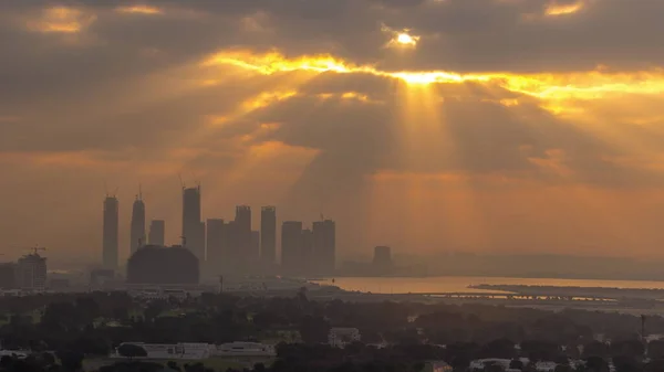 stock image Sunrise over Dubai Creek Harbor with skyscrapers and towers under construction aerial timelapse. Cloudy orange sky with sun beams