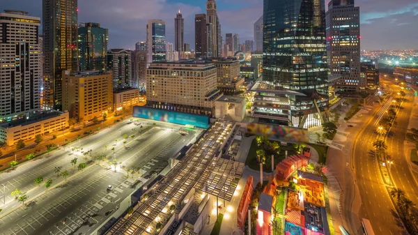Dubai International Financial district night to day transition timelapse. Panoramic aerial view of business office towers and parking lot before sunrise. Illuminated skyscrapers with hotels and shopping mall