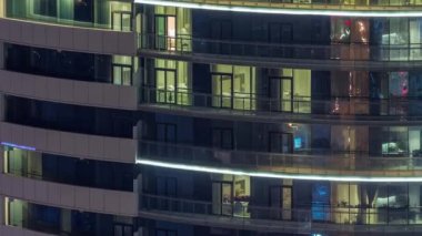 Modern konut binalarındaki büyük parlayan pencereler geceleri zaman ayarlı, sıra sıra parlıyor. Görüntüyü kapat