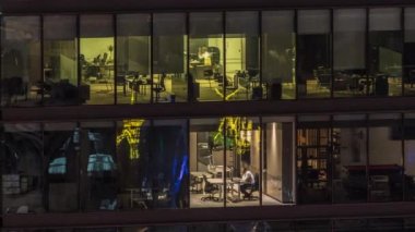 Modern ofis binalarındaki büyük parlayan pencereler geceleri zaman ayarlı, sıra sıra parlıyor. İçerideki bilgisayarlarda çalışanlar