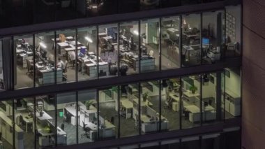 Modern ofis binalarındaki büyük parlayan pencereler geceleri zaman ayarlı, sıra sıra parlıyor. Açık alan çalışma yerleri