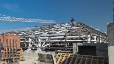 Üniformalı müteahhitler ve marangozlar çatıda çalışıyor. Modern binaların sarı vinçleri olan bir inşaat alanı. Çatıdan arkaplan görünümünde mavi bulutlu gökyüzü