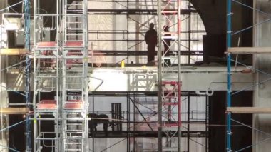 İnşaat malzemeleri iskeleli ve aletleri yüksek binanın zemininde, zaman tünelinde, gökdelende. İnşaat devam ediyor. Katlar arasında iç çalışma devam ediyor.