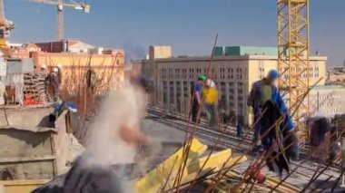 İnşaat alanındaki vinçlerle beton takviyesi için çelik çubuk inşaat iskeleti takviyesi. Üniformalı birçok işçiyle birlikte yeni bir binanın çatısında metal çalışıyor.