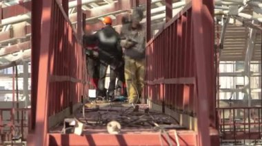 Welders working with electrode at semi-automatic arc welding metal reinforcement on a construction site timelapse. Workers in uniform and scaffolding on metal bridge