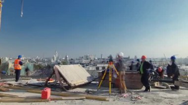 İnşaat alanındaki panoramik zaman diliminde beton için çelik çubuk inşaat iskeleti takviyesi. Crane, üniformalı birçok işçiyle birlikte yeni bir binanın çatısında çalışıyor.