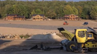 Manzara kentsel zaman dilimine dönüşür. Büyük bir tarladaki yeni kır köyü için buldozerle inşaat alanındaki ahşap evlere bakın..