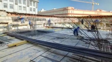 İnşaat alanında beton takviyesi için çelik çubuk inşaat iskeleti takviyesi. Metal teller yeni binanın çatısında çalışıyor. Üniformalı birçok işçi çalışıyor.