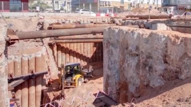 A large huge ditch pit tunnel timelapse with crane and excavator. Reinforcing structures from thick iron pipes of beams and structures at the construction site of the underground metro station line.