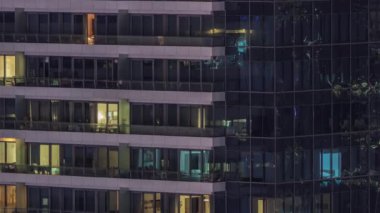 Geceleri modern binalardaki pencere ışıkları zaman ayarlı. İçinde aydınlık odalar olan çok katlı gökdelenler.