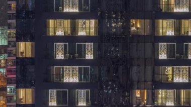 Modern ofisteki pencere ışıkları ve geceleri konut binaları. İçinde aydınlık odalar olan çok katlı gökdelenler. Balkonda birkaç sandalye.